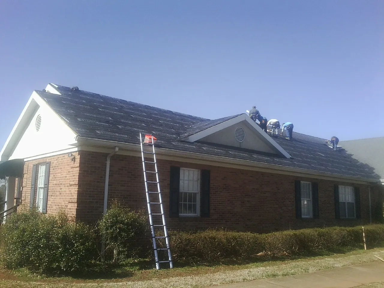 Crew tearing shingles off a brick ranch roof with a ladder set — Metal Roof Repair work by our crew in Chocorua