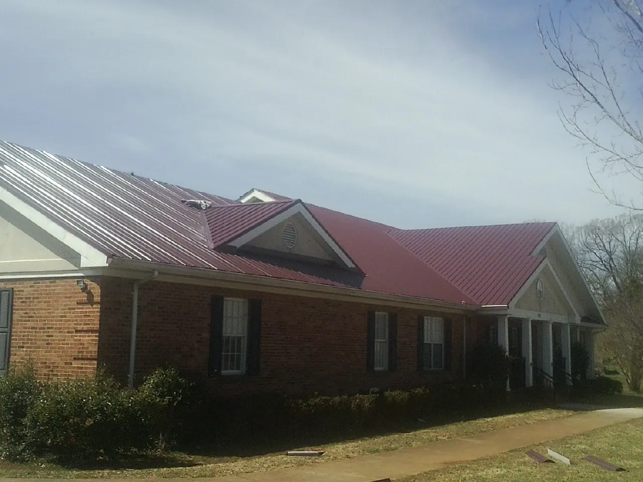 Red metal roof with gabled entries on a long brick building, from a Hail Damage Roof Repair job in Chocorua