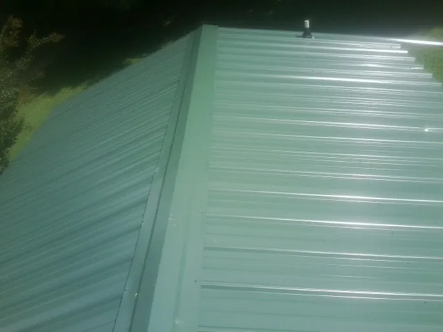 New green metal panels meeting at the ridge of a roof — Flat Roof Repair work by our crew in Chocorua