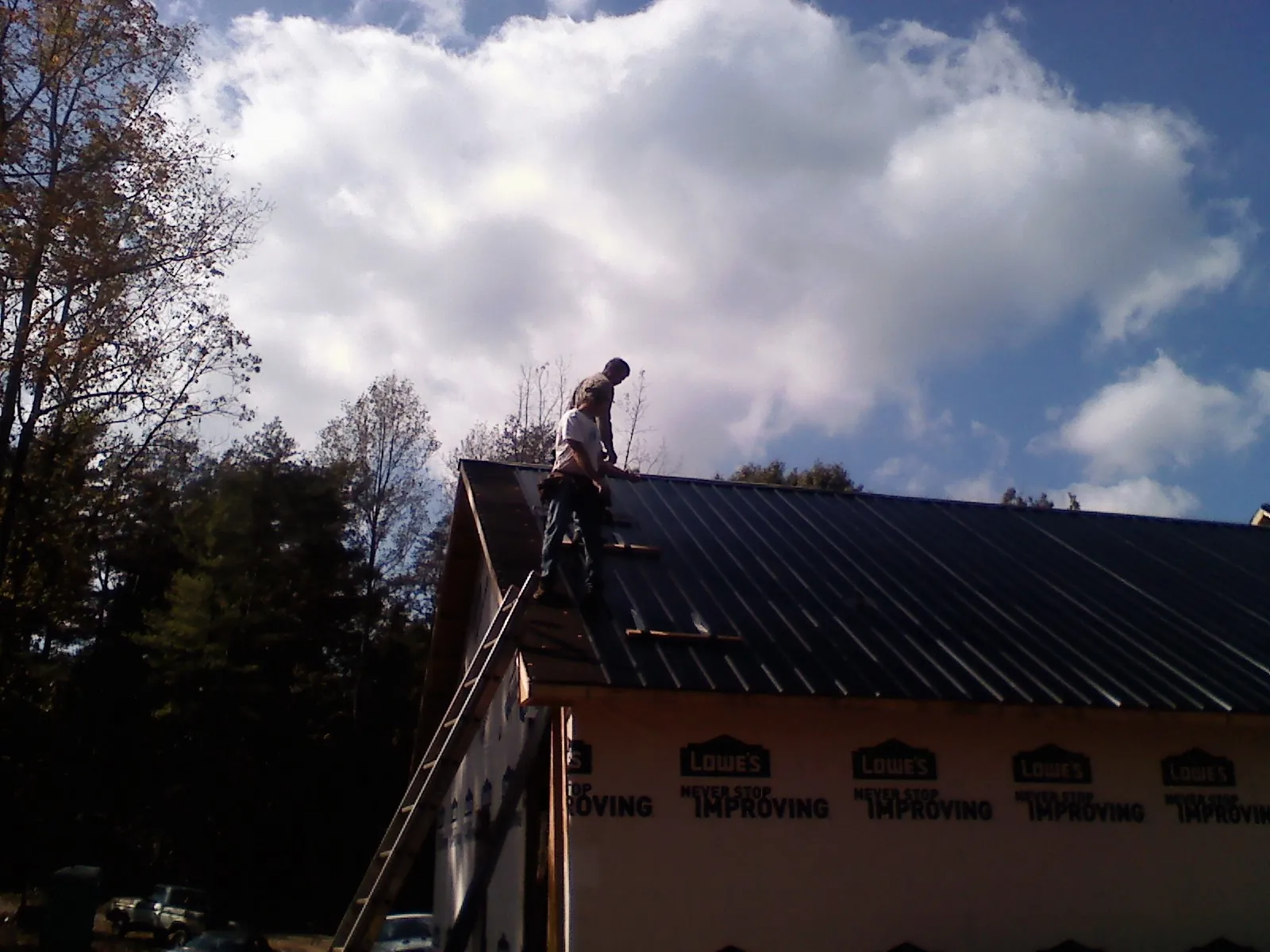 Roofer fastening dark metal panels high against a cloudy sky, from a Roof Inspection job in Chocorua