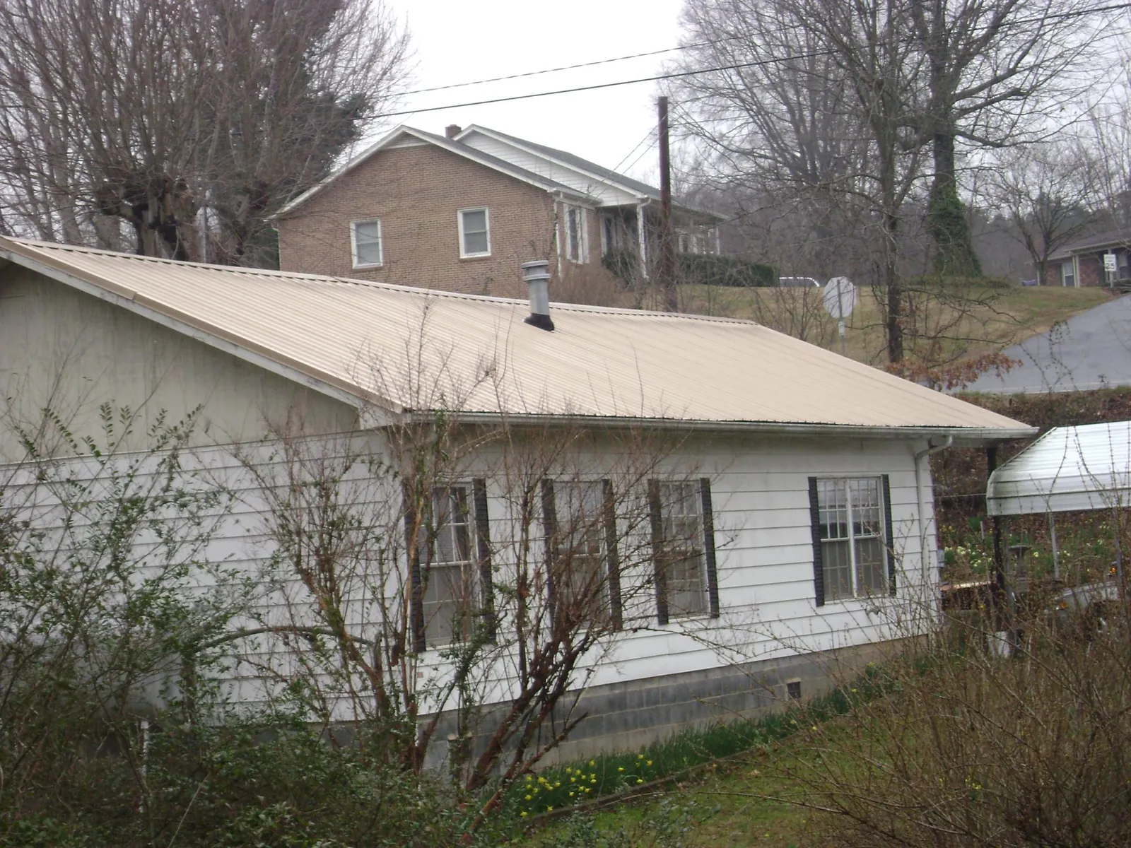 Tan metal roof on a white sided house set into a hillside — Commercial Roofing by Roofing Brothers in Chocorua